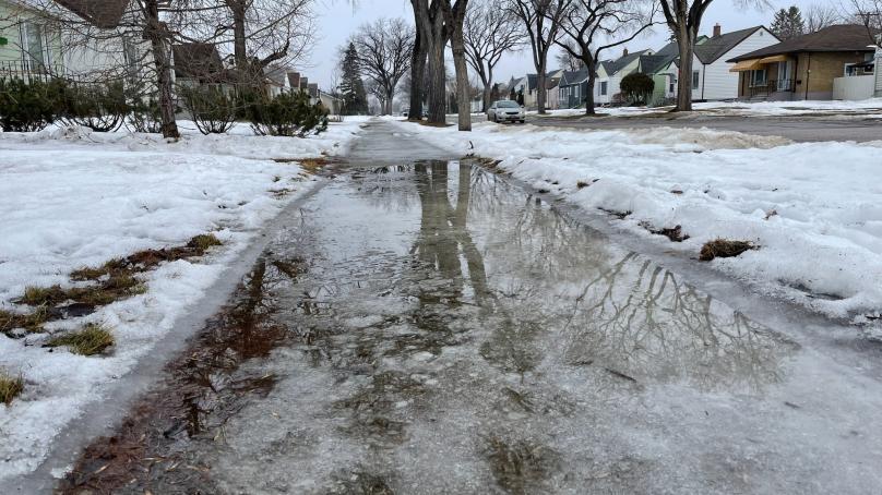Water pools over an icy sidewalk on a residential road.