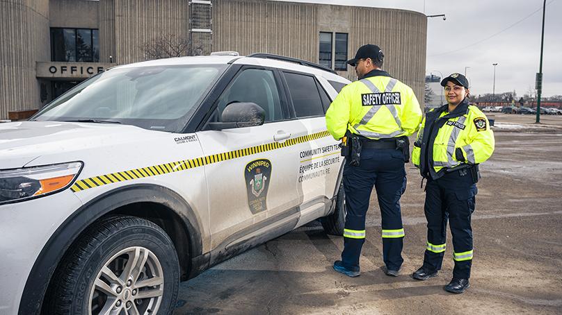 Two Community Safety Officers stand next to a vehicle.
