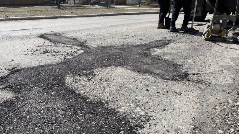 Crews stand near a newly patched pothole.
