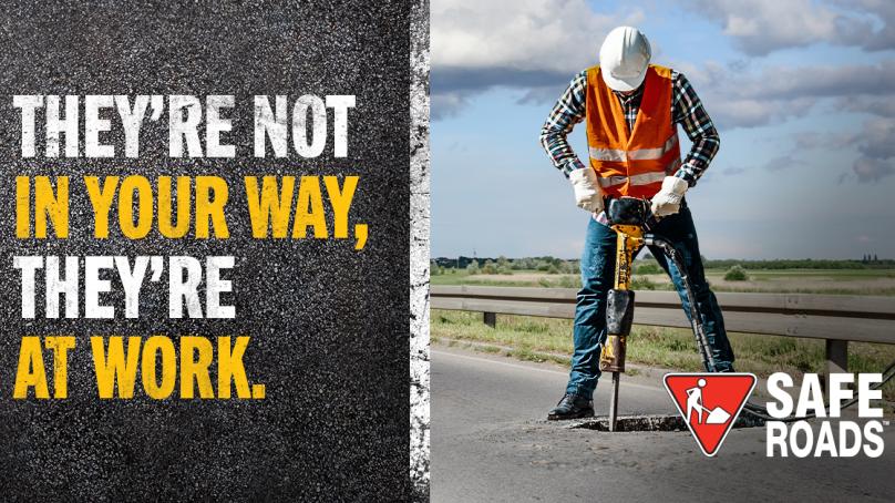 A man in a high visibility vest uses a drill on a road. A message on the left says, "They're not in your way, they're at work."