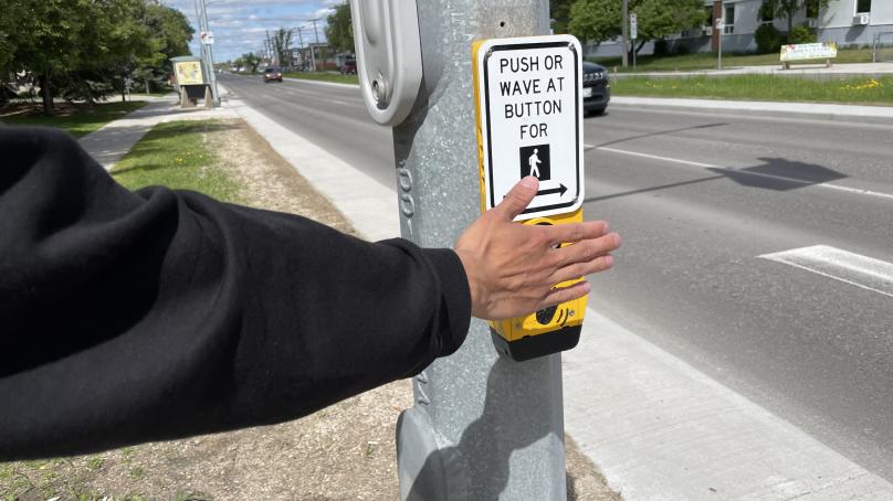 A person's hand touches a pedestrian push button at a crossing.