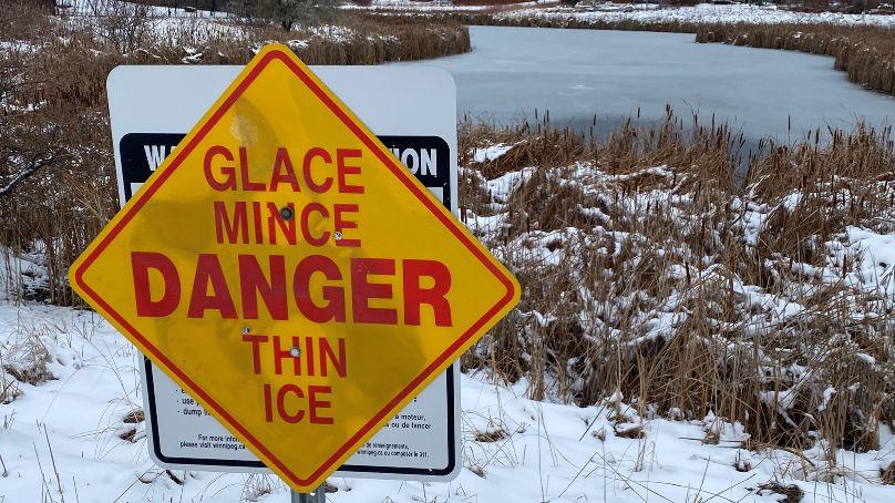 Thin ice sign in front of partially frozen waterway