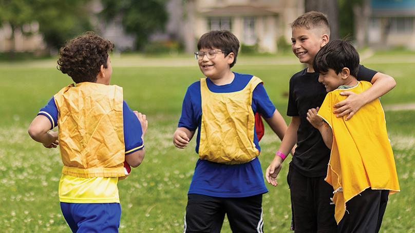 Happy boys wearing yellow pinnies gathered during soccer game outdoors at camp