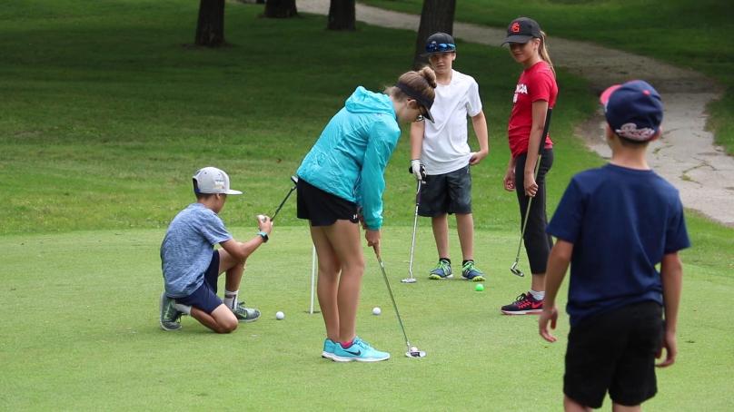 Several kids gathered on a golf course, preparing their shots.