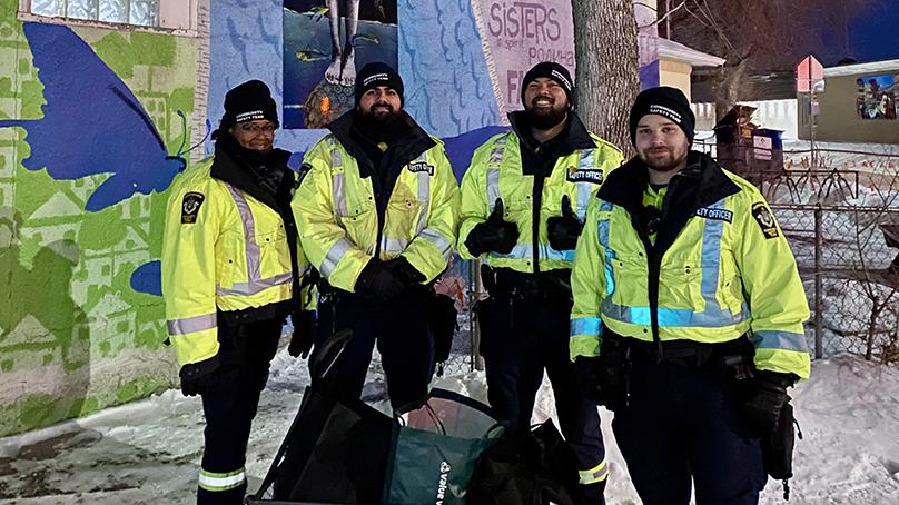 Four Community Safety Team members standing at night outside in front of a painted wall