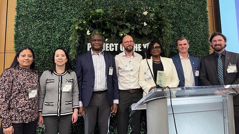 Group of people standing on stage holding an award shaped like the province of Manitoba