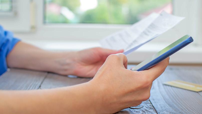 Hand holding a cell phone with paperwork around it