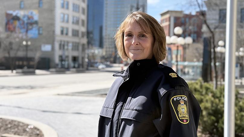 Police office (Ins. Helen Peters) standing outside in front of downtown skyline.