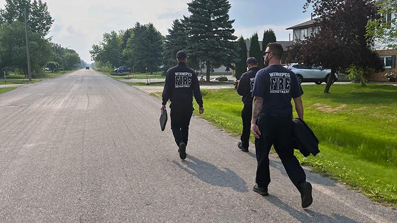 Group of people walking down a residential street wearing Winnipeg Fire Paramedic Service clothing.