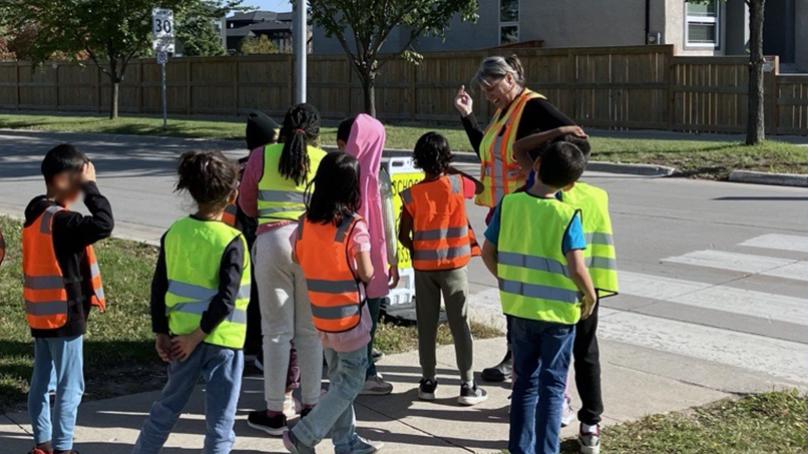 Children wearing safety vests standing at a crosswalk