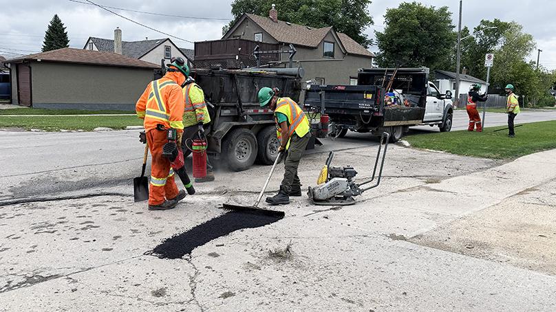 Workers in safety gear filling potholes and straightening a sign
