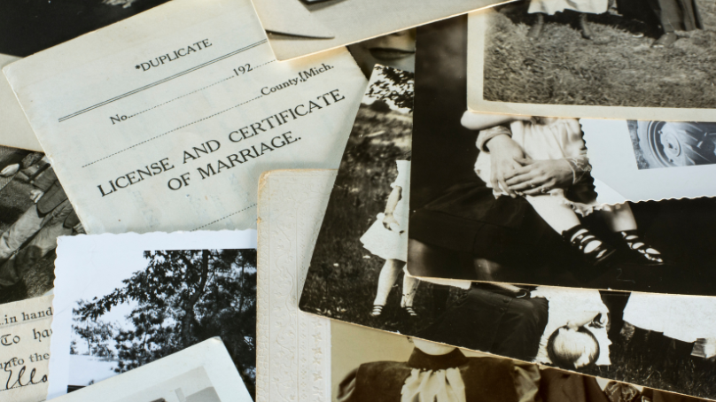 A pile of old photographs and a marriage certificate sit on a table. 