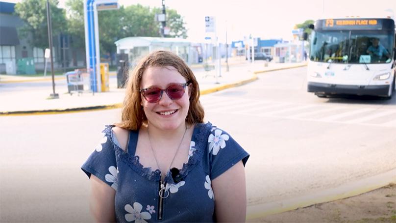 Woman standing at a bus stop with a bus behind her.
