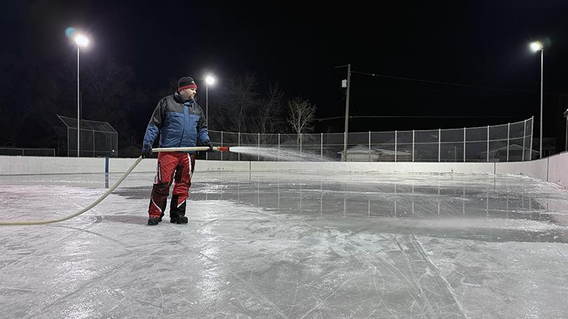 A person floods an outdoor rink during winter.