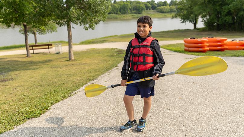 Older child standing beside water holding a paddle