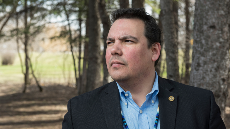Niigaan Sinclair, writer, editor and professor, standing amongst trees.
