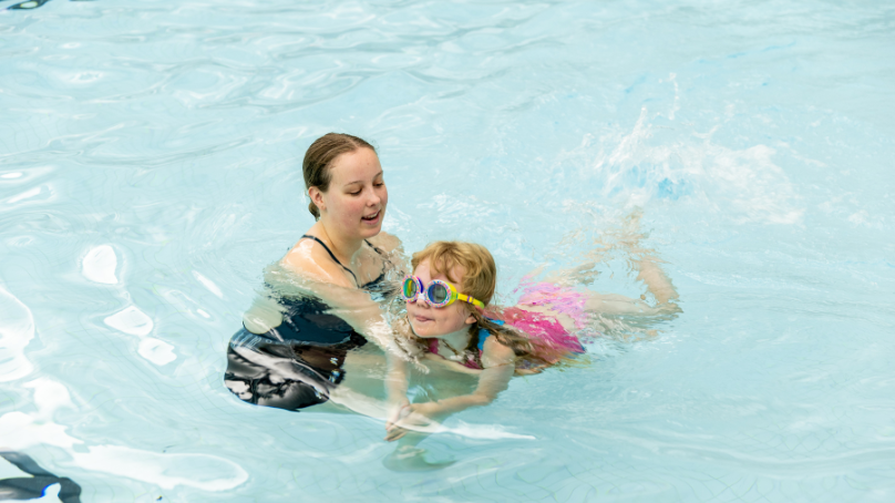 Child in a pool being assisted by a swim instructor