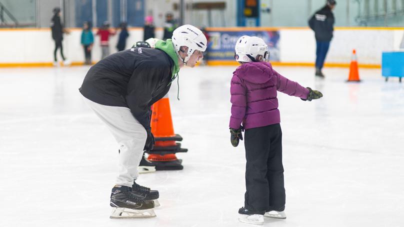 Skating instructor crouching down listening to skater who is pointing to the right