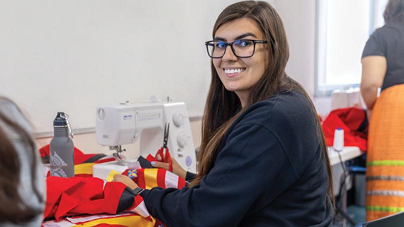 Smiling woman seated at sewing machine with a red ribbon skirt