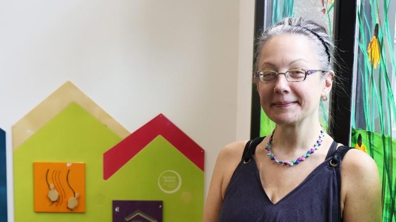 Maker-in-Residence, Maureen Winnicki Lyons standing against a mural on the main floor of Millennium Library.