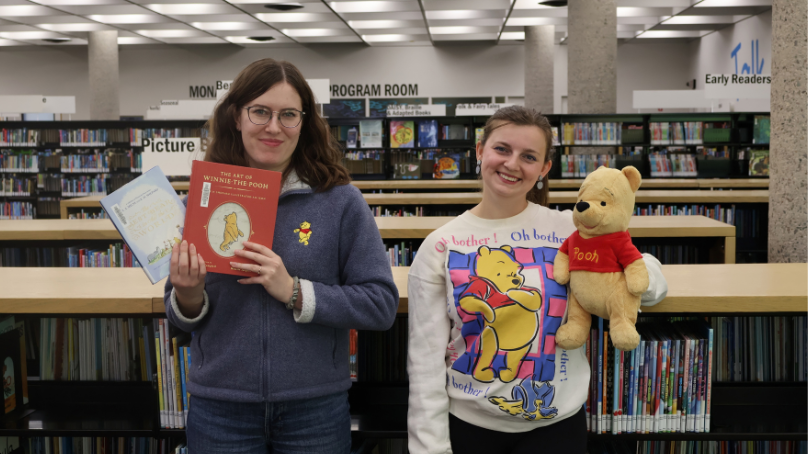 Winnipeg Public Library staff holding Winnie-the-Pooh books and a puppet inside a library