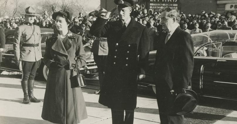 Royal Tour, Winnipeg, October 16, 1951. Princess Elizabeth, Duchess of Edinburgh (later Queen Elizabeth II) and the Duke of Edinburgh (or Prince Philip) stand on a sidewalk near the Paris Theatre on Provencher Blvd. City of Winnipeg Archives.