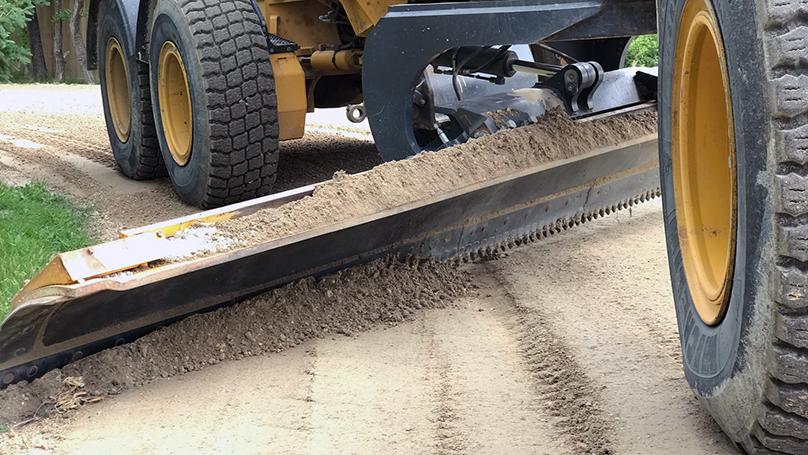 A grader blade down on a gravel road.