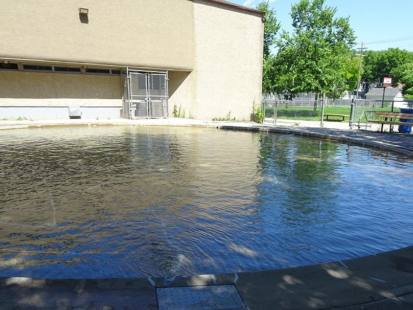 Wading pool full of water with Luxton Community Centre in the background