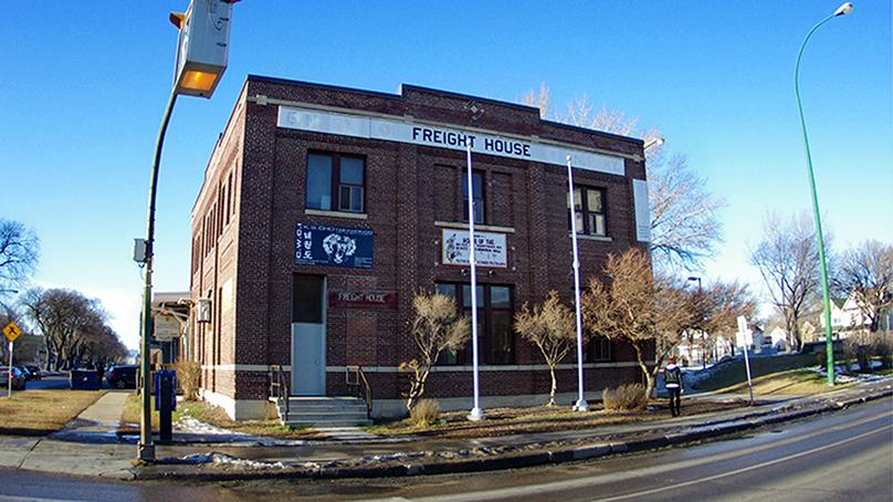 Streetfront brick building of Freight House on a sunny day with some snow on the ground green grass and bare trees