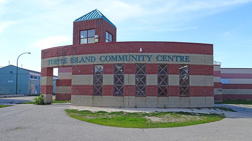 Curved building with horizontal stripes of bricks in a sand colour and terracotta colour. Green text on building says Turtle Island Community Centre. 