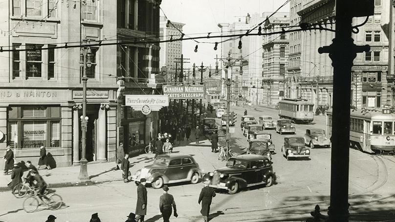 Portage Avenue and Main Street with pedestrians, bicycles, and vehicles in view. Credit: University of Manitoba Archives & Special Collections